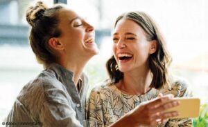 Woman holding mobile phone with freind, laughing